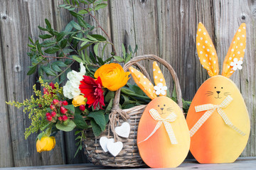 Zwei Osterhasen aus Holz mit einem Blumenstrauß im Weidenkorb als Dekoration zu Ostern