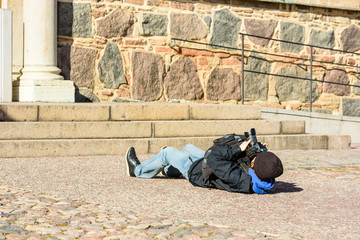 Photographer lying on the ground while photographing a large building from different perspective. Creative photography style.