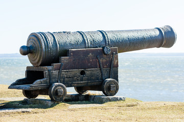 Old, antique cast iron canon pointing out at sea from a defensive wall.