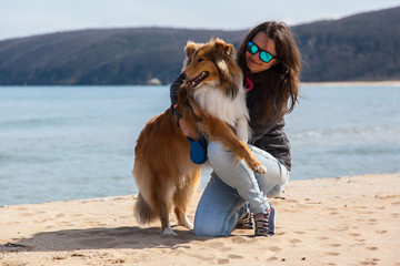 Young girl in blue sunglasses hugging a dog (scottish collie) on the beach on Black sea on a sunny...