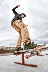Fototapeta na wymiar Teen skater in a hoodie sweatshirt and jeans slides over a railing on a skateboard in a skate park