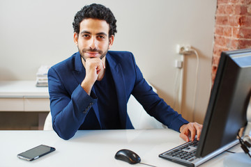 An Arab  businessman in a jacket sitting on workplace behind computer in office