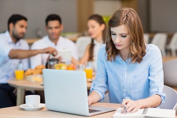 Businesswoman working on laptop while having coffee