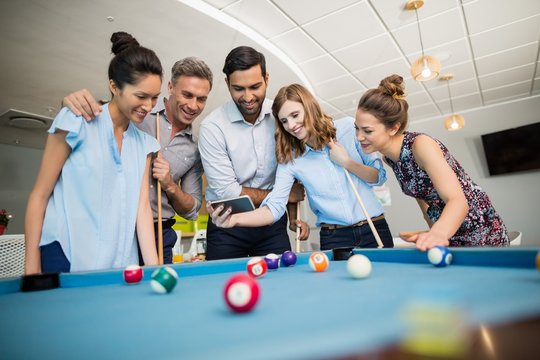 Colleagues using phone while playing pool in off