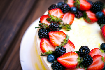 Birthday  lemon cake with strawberries, blueberries and blackberries on a dark wooden board