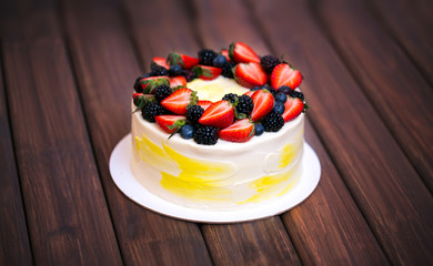 Birthday  lemon cake with strawberries, blueberries and blackberries on a dark wooden board