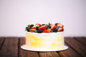 Birthday cake with strawberries, blueberries and blackberries on a dark wooden board