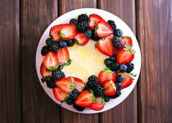 Birthday  lemon cake with strawberries, blueberries and blackberries on a dark wooden board. Top view..
