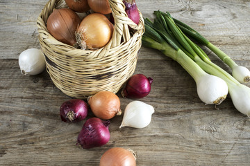 Different onions in basket on wooden table