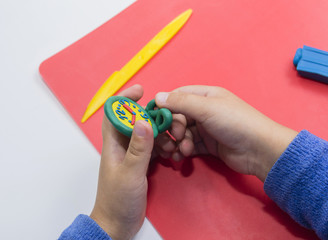 Cropped Child's Hand Making Clock With Modelling Clay On White and Red Table