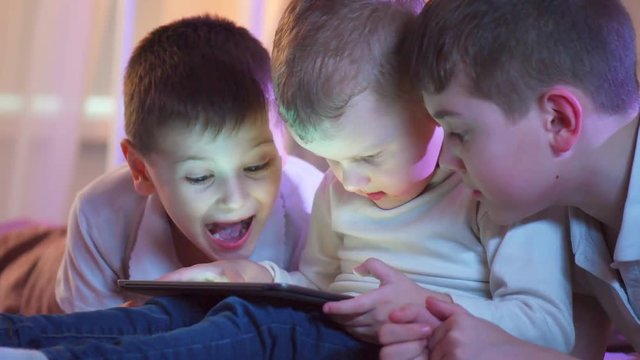 Three little boys with tablet computer in a dark room. Kids playing games on tablet pc. 4K UHD video
