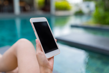 Young Woman using cellphone and lying besides swimming pool