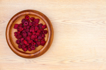 Healthy food. Wooden plate with fresh raspberry in it and wooden spoon isolated on beige background. 