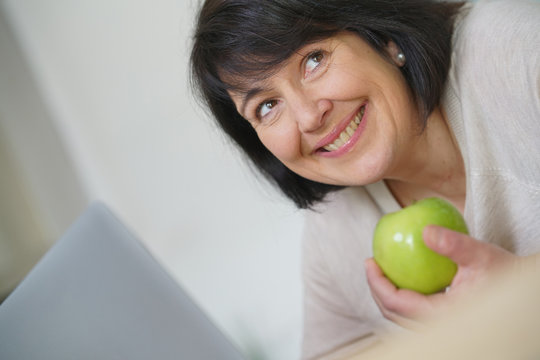 Cheerful mature woman eating green apple