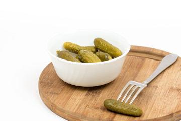 Small pickles in the white bowl and pickle on the fork