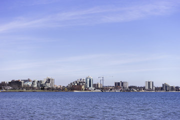 Naklejka premium Low urban skyline across a blue water, large sky, background space for text