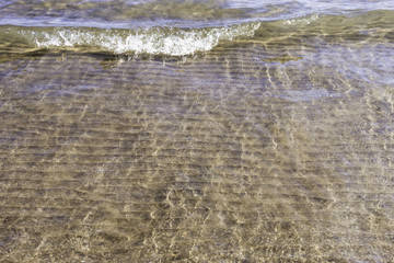 Wave breaking onto calm sandy beach, clear fresh water, background space for text