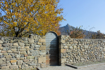 Old stone wall with iron door in autumn. Region Mtsketa, Georgia. The ancient monastery Jvari on...