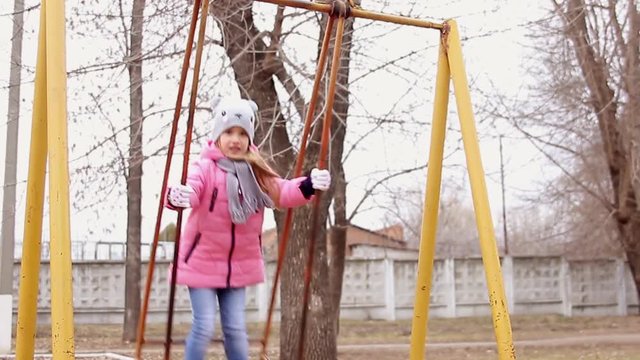 Little girl on swing in city park, happy child on swing. Concept girl in pink on a swing quickly. Child, Playing, Playground.
