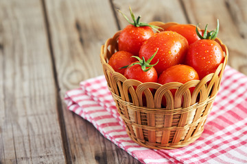 Fototapeta na wymiar Fresh cherry tomatoes in woven basket on wooden background. Copy space