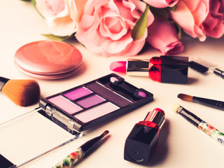Obraz na płótnie Canvas Make up products lipstick, blush eye shadows and tools brushes with pink roses flowers on white background. Lifestyle woman still life