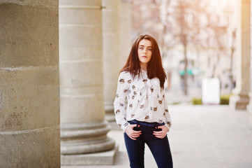 Fototapeta premium Young stylish brunette girl on shirt and pants posed near stone columns. Street fashion model concept.