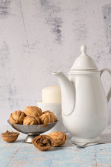  Dessert for coffee. Homemade pastry in the form of nuts in an old metal vase, a tall coffee pot with hot coffee and a candle in a white porcelain candlestick on a light wooden table.