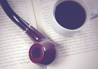 red wooden pipe on open book with coffee cup