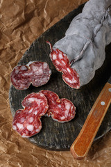 Sausage salami and knife on beige paper top and side view. Sausage sausage with ashes. French country sausage. Rustic food still life