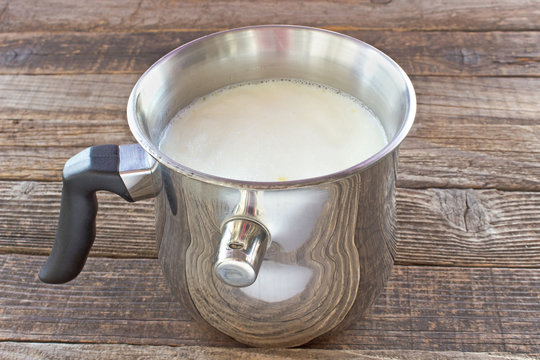 Hot milk boiled in metal pot with whistling alarm on wooden table
