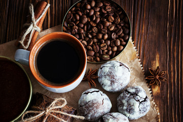 Chocolate cookies and cup of coffee with coffee bean, cocoa powder, cinnamon and star anise on wooden table.