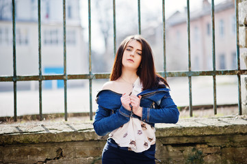 Fototapeta premium Young stylish brunette girl on shirt, pants, jeans jacket posed background iron fence. Street fashion model concept.