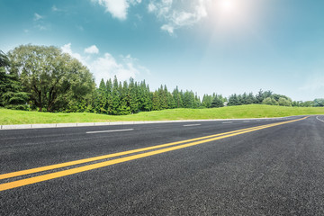 Fototapeta premium Asphalt road and green trees in the blue sky