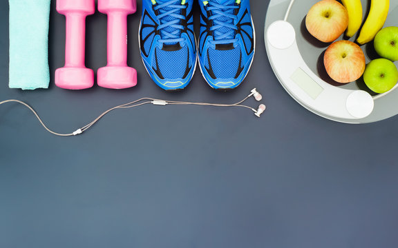 Fitness and weight loss concept, sport shoes, dumbbells, towel, earphone, weighting scale, apples, bananas, top view with copy space
