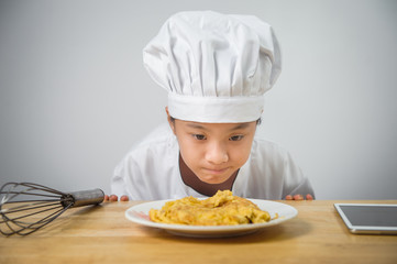 Kids chef is looking at the omelet in the dish,have a taplet on table