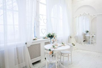 Interior design of white room with beautiful flowers on the served table. Big windows and creative classical mirror at the background. Horizontal