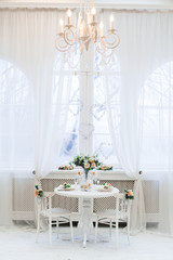 Interior design of white room with beautiful  flowers on the served table. Big windows and creative classical mirror at the background. Horizontal