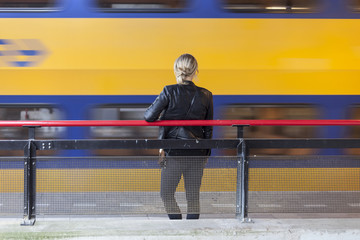 young woman waits on platform of railway station in holland while train passes