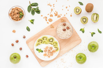Healthy breakfast with yogurt, muesli, fresh green fruits, cereal, nuts on white background. Flat lay, top view.