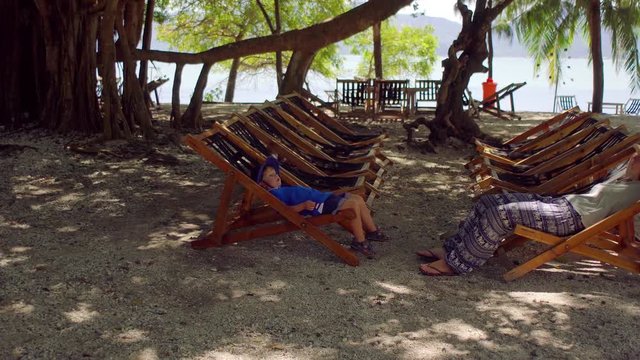 Woman and son sitting in chaise-lounges under a big tree. Monkey Island. Nha Trang. Vietnam