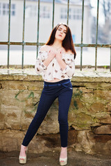 Young stylish brunette girl on shirt, pants and high heels shoes, posed background iron fence. Street fashion model concept.