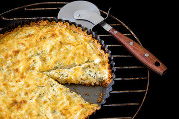 Sliced homemade quiche with chicken, cheese and green onion and parsley and Pizza knife on black...