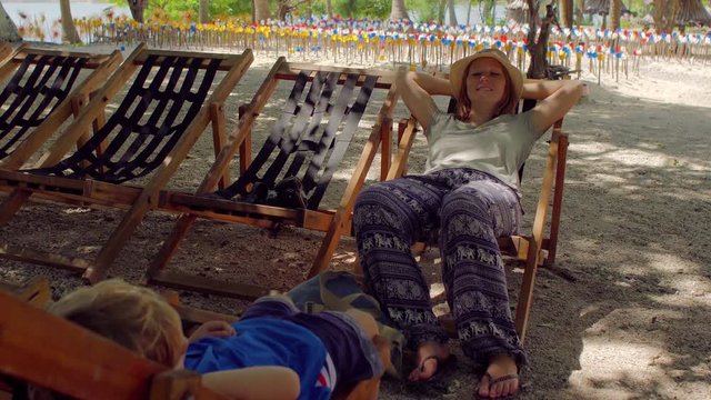 Woman and son sitting in chaise-lounges under a big tree. Monkey Island. Nha Trang. Vietnam