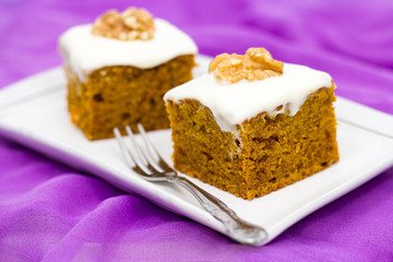 Two pieces of homemade carrot cake with orange, zest, walnut and icing cream, on the lilac background. Selective focus