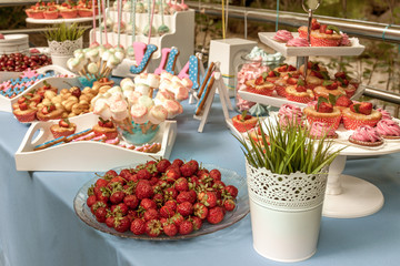 Seven little kids sit at red table with cake and throw confetti at birthday party. Inscription Happy Birthday on wall