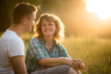 Beautiful senior woman and her adult smiling son sitting in park