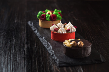 Side view on mini party tartlets with fresh fruit, chocolate, nuts and cream on black slate background