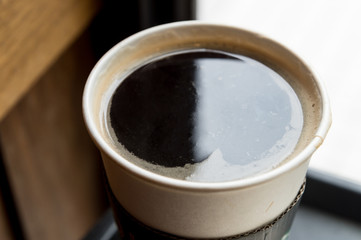 Close up hot black coffee cup on wood table top at coffee shop window.