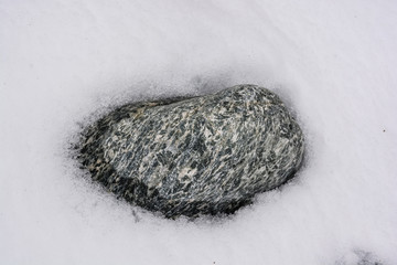 Close up grey stone lies in snow in nature pattern