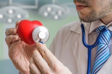 Cardiologist doctor is listening red heart with stethoscope.